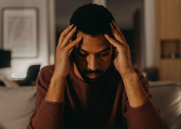 Man feeling stressed and upset indoors after his girlfriend publicly claps back and ends their relationship.