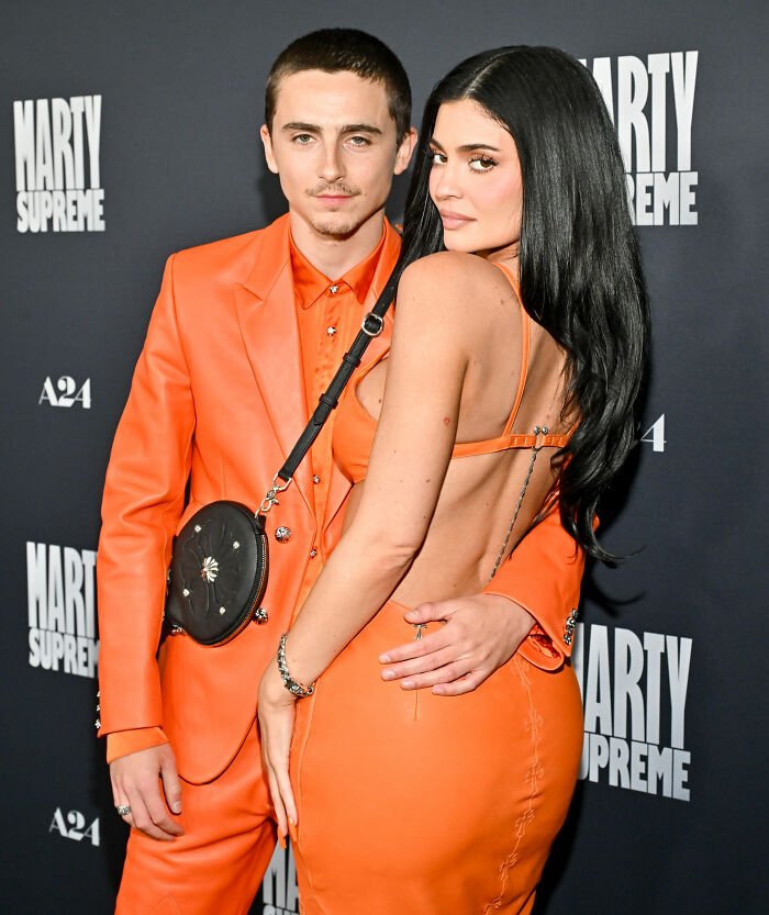 Timothée Chalamet and Kylie Jenner posing together on red carpet, both wearing coordinated orange outfits.