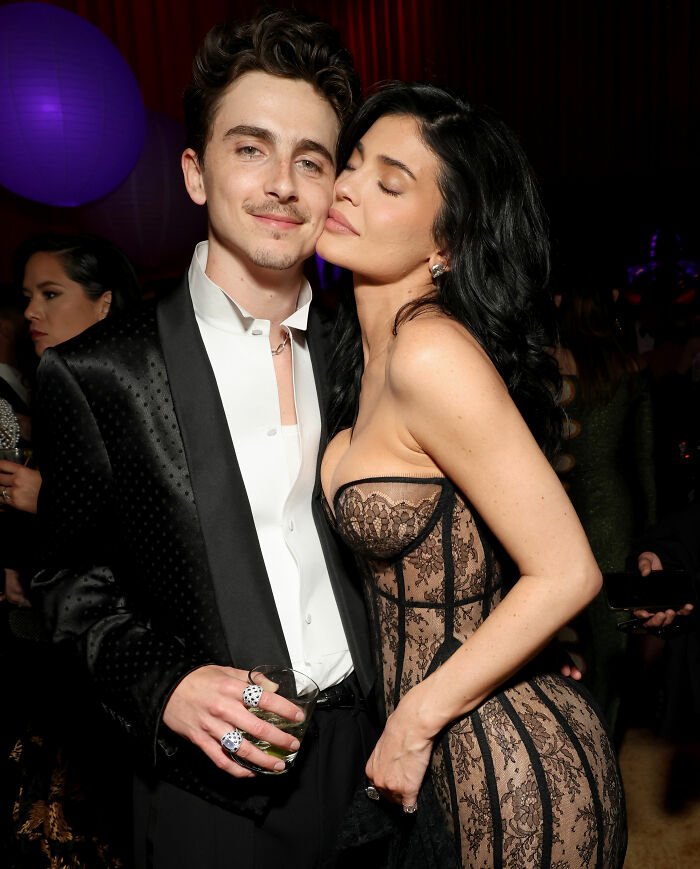 Timothée Chalamet in a black tuxedo and Kylie Jenner in a lace dress posing together at a red carpet event.