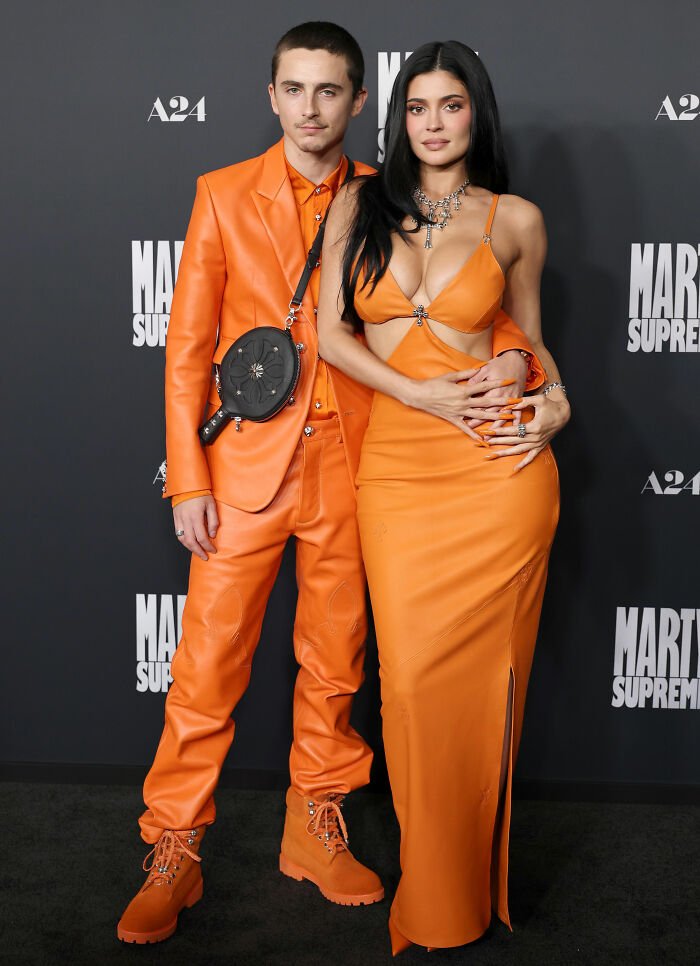 Timothée Chalamet and Kylie Jenner on the red carpet wearing matching orange outfits with a unique fashion detail.