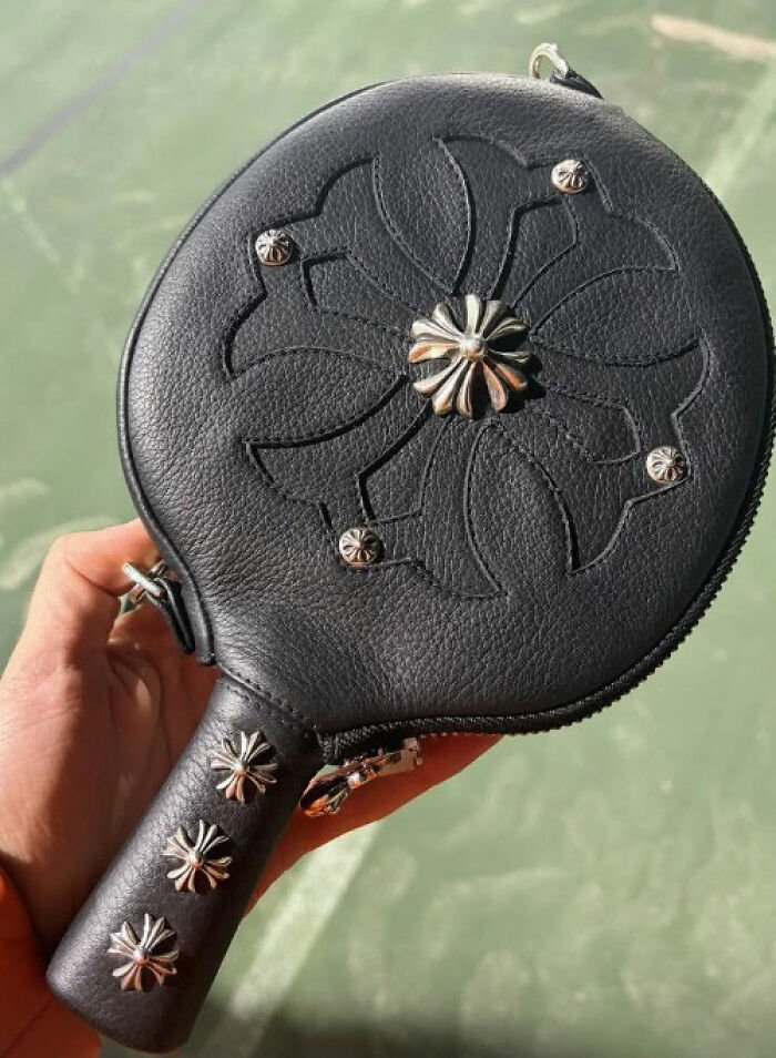 Black leather handbag with metal flower studs in a hand, linked to Timothée Chalamet's red carpet look odd detail