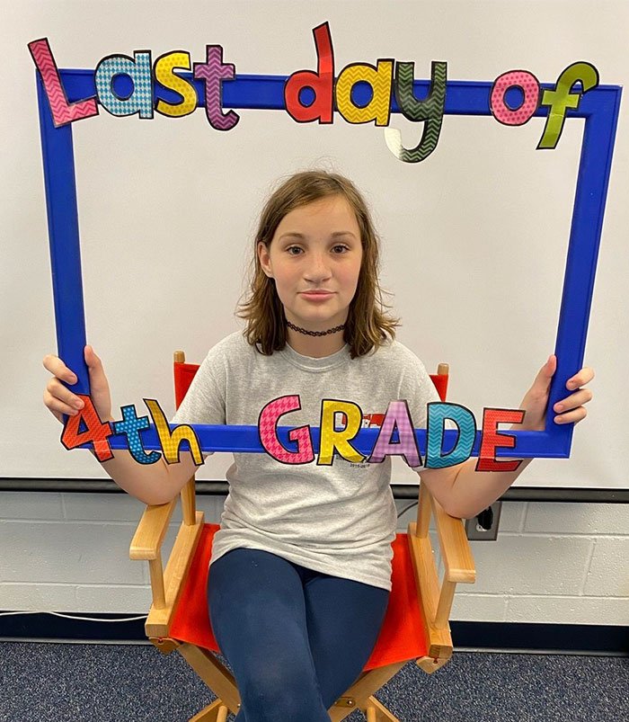 Young girl holding a colorful last day of 4th grade frame, highlighting accused teens luring tactic in disturbing woods incident