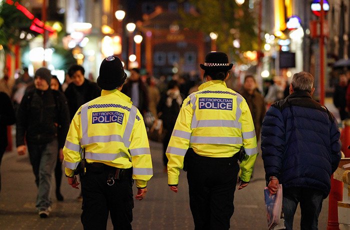 Two metropolitan police officers walking in a crowded urban area investigating wealthy US student behavior after altercation.
