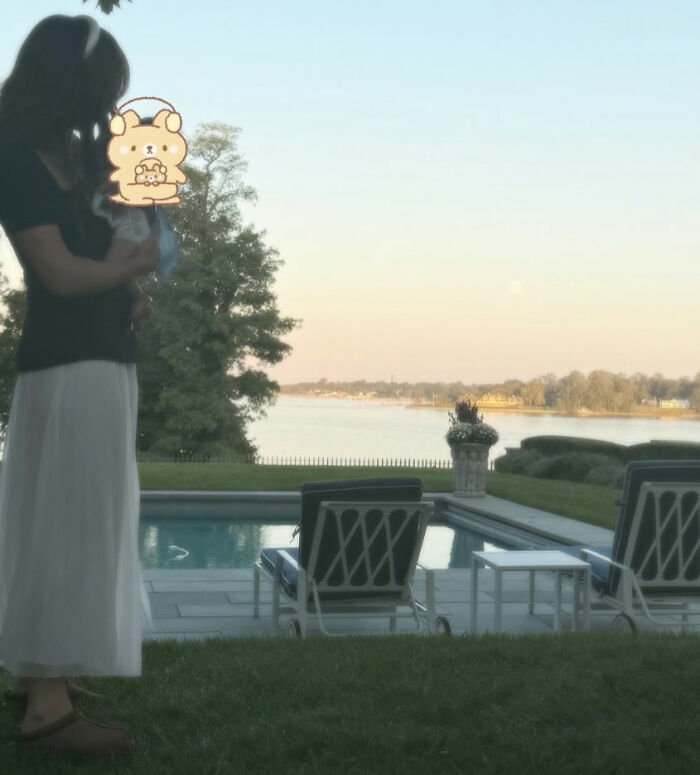 Woman holding newborn by poolside with scenic lake view, related to Millie Bobby Brown newborn daughter viral theory.