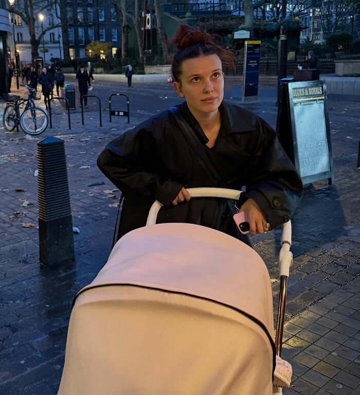 Millie Bobby Brown pushing a stroller outdoors at dusk, sparking viral theory about her newborn daughter after new pics.
