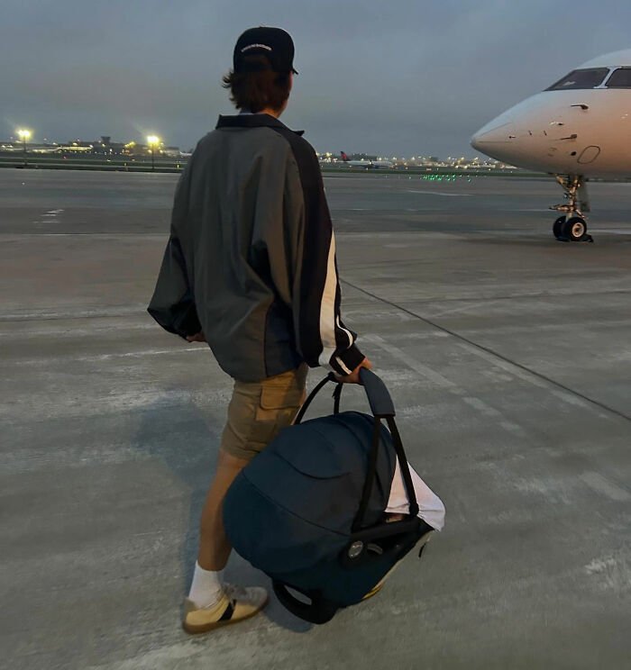 Person carrying a car seat at an airport tarmac at dusk, related to viral theory about Millie Bobby Brown's newborn daughter.