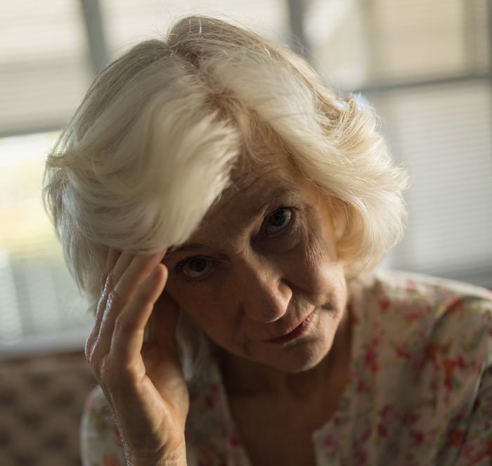 Elderly woman looking distressed indoors, highlighting women ruining MIL&rsquo;s surprise by pretending ignorance.