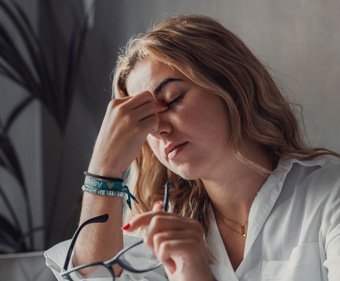 Woman holding glasses and rubbing her forehead looking stressed after women ruin MIL&rsquo;s surprise event.