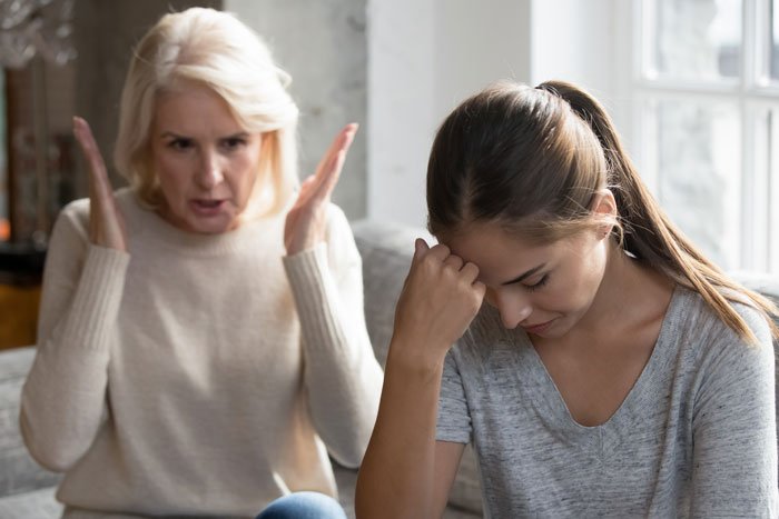 Two women in a tense moment indoors, with one appearing frustrated and the other upset, illustrating a family surprise gone wrong.