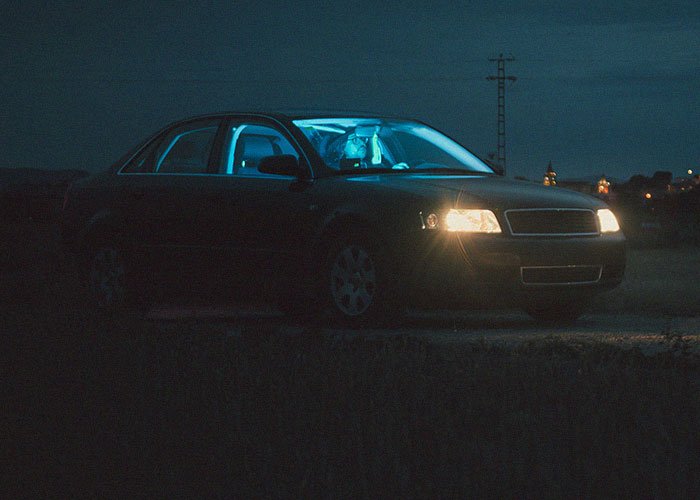 Person inside a dark car at night, appearing distressed and held hostage at their parents’ place, unsure of what to do.