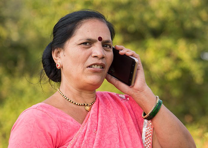 Woman in pink sari holding phone, appearing concerned, illustrating being held hostage at parents’ place situation.