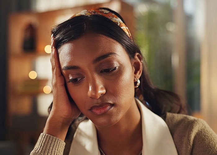 Young woman looking distressed and worried, sitting indoors, depicting the feeling of being held hostage at parents’ place.