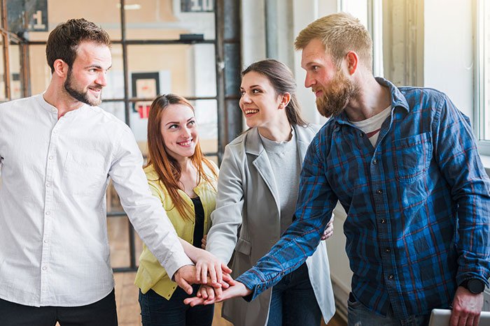 Group of coworkers joining hands in teamwork gesture, illustrating subtle red flags that mean job insecurity.