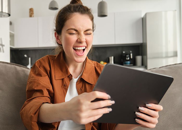 Young woman at home reacting upset while holding a tablet, relating to son’s partner gift conflict and tacky trinkets issue.