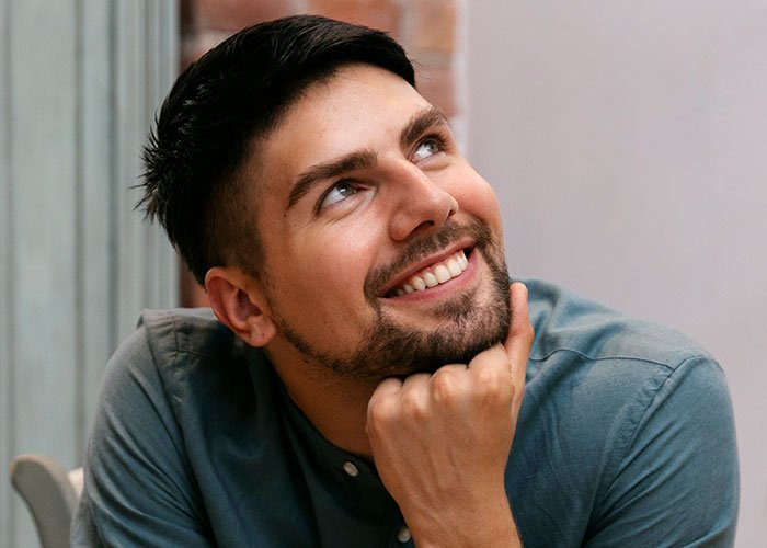 Young man smiling thoughtfully, reflecting on a woman upset about her son’s partner not bringing a gift.