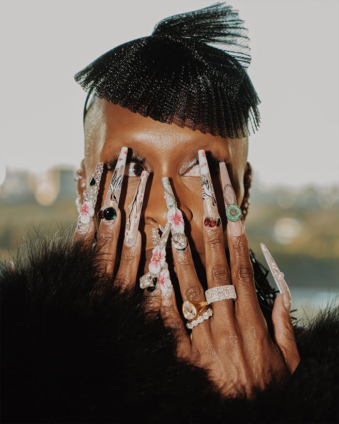Cynthia Erivo showing off oddly large hands with long floral nails and rings, sparking fashion and beauty debate.