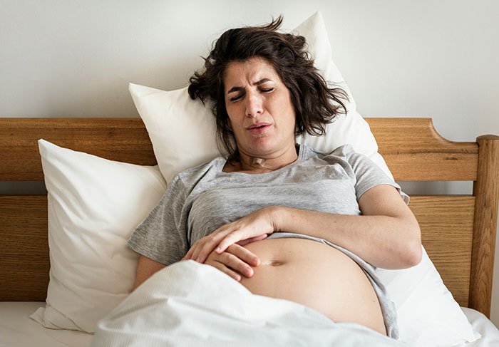 Pregnant woman in pain lying in bed, depicting challenges faced by a childfree woman refusing responsibility for new baby.