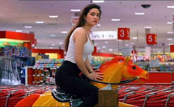 Jennifer Connelly sitting on a bright orange horse ride inside a store, reflecting on iconic movie scene regrets.