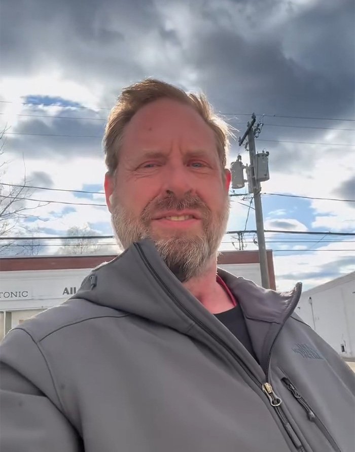 Middle-aged man with beard wearing a gray jacket standing outdoors under a cloudy sky, discussing ChatGPT controversy.