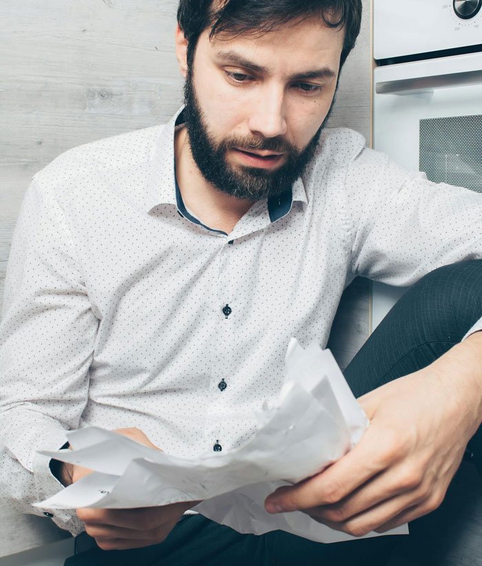 Man with beard sitting on the floor, reading documents and looking worried about divorce and relationship issues.