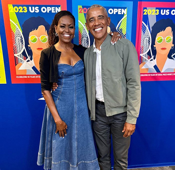 Michelle Obama and Barack Obama smiling together at the 2023 US Open event with colorful tennis posters in the background