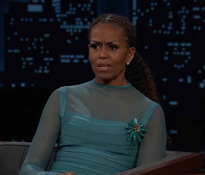 Michelle Obama speaking seriously during a televised interview with a cityscape background at night.
