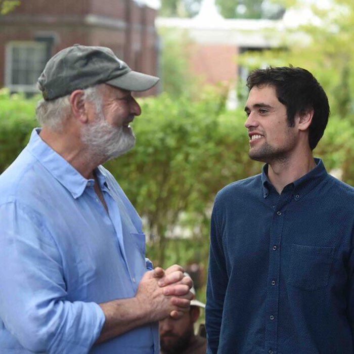 Two men smiling and talking outdoors, captured in a candid moment about Michelle Obama and Trump news.