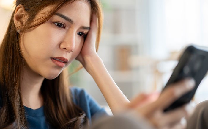 Young woman looking concerned while holding a smartphone, reflecting on a guy mocking girlfriend for playing video games.