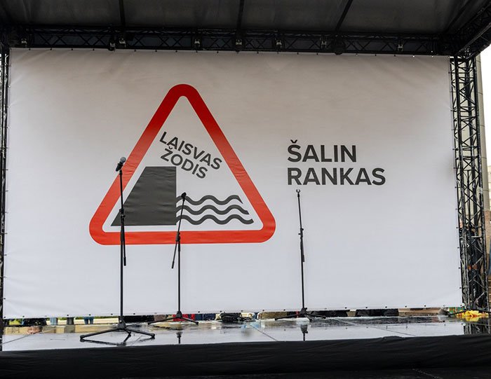 Outdoor stage with microphones and a banner featuring a protest sign related to Lithuania lawmaker’s cat consent.