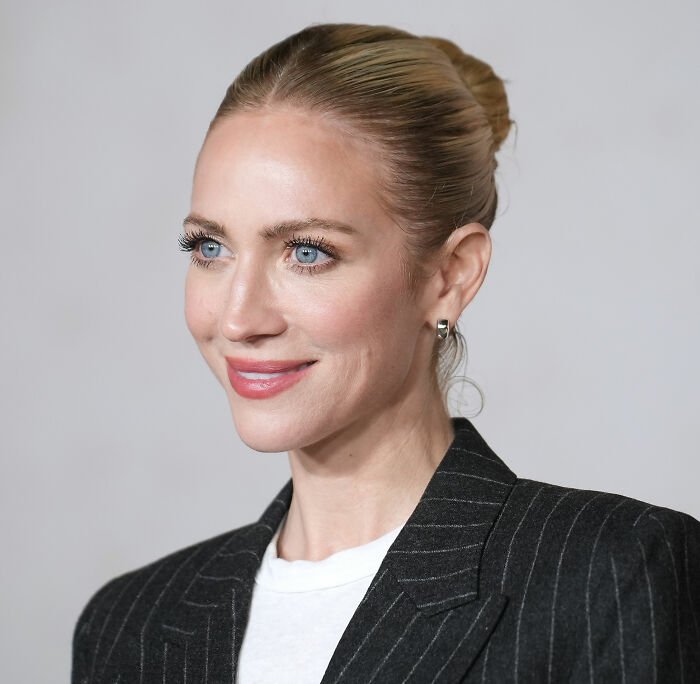Britanny Snow smiling with hair in a bun, wearing a pinstripe blazer and white shirt against a plain background.