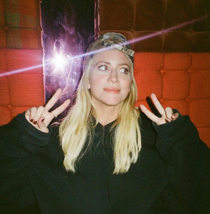 Britanny Snow posing indoors with peace signs, wearing a black hoodie and a cap, addressing plastic surgery rumors.