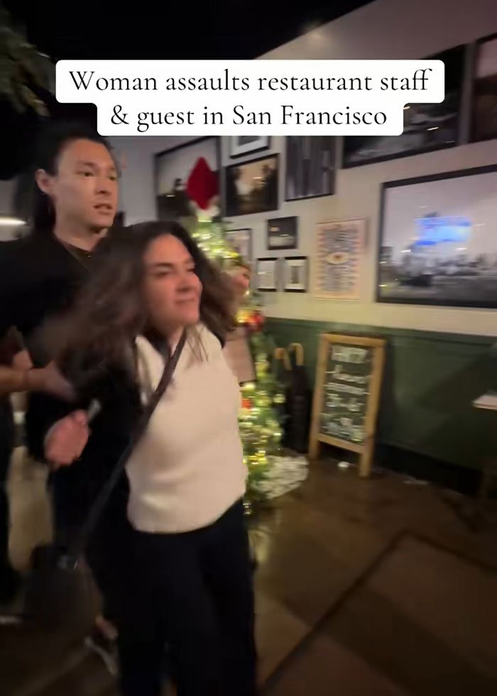 Woman involved in drunken rampage at upscale restaurant being restrained inside a decorated dining area at night.