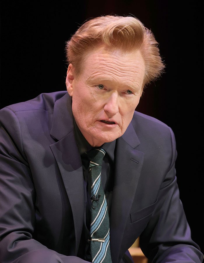 Conan O'Brien speaking in a dark suit and striped tie during a televised interview about celebrities and unusual questions.