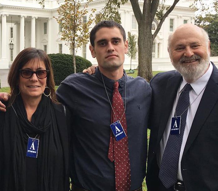 Rob Reiner&rsquo;s children Jake and Romy posing outdoors with an older man near a white building, wearing appointment badges.