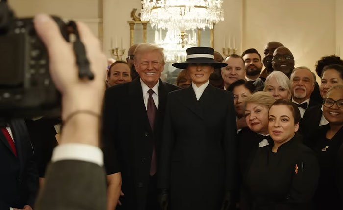 Photographer capturing Melania Trump and Donald Trump posing with a group of people in an elegant room.