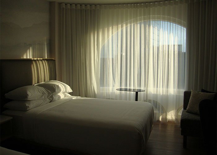 Minimalist hotel room with a neatly made bed and sheer curtains, evoking intimate encounters and K-drama-style dates.