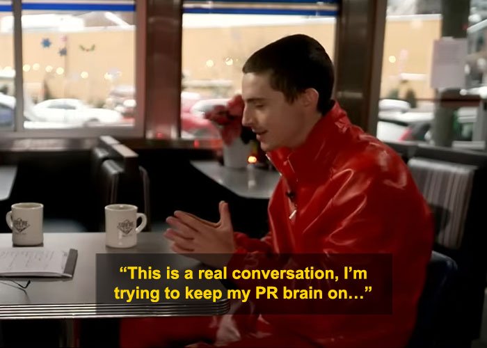 Timothée Chalamet in red jacket during interview, facing criticism for perceived arrogance in public appearance.