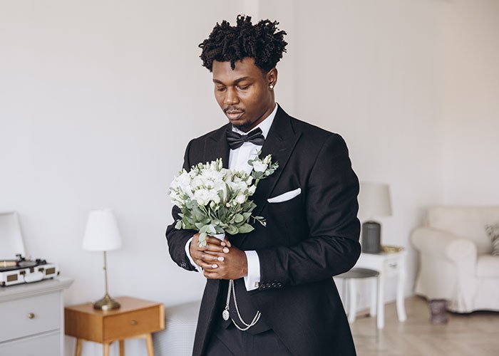Man in tuxedo holding wedding bouquet, appearing thoughtful and waiting before wedding day without closure.