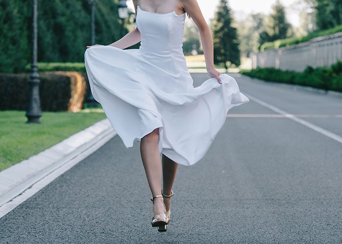 Bride in white dress running away on empty road symbolizing fianc&eacute; disappears before wedding and man left without closure.