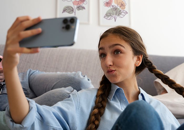 Young woman taking a selfie on smartphone, upset over sister building TikTok fame by lying about her in family setting.