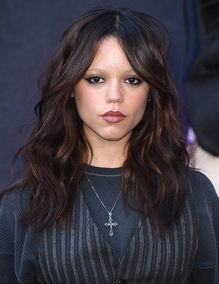 Young female celebrity with dark wavy hair and bold makeup wearing a cross necklace, representing beauty with golden ratio standards.