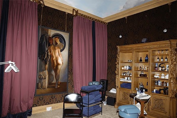 Dimly lit room with ornate cabinet, stacked towels, and a painting, linked to chilling toddler's foot beside Epstein.