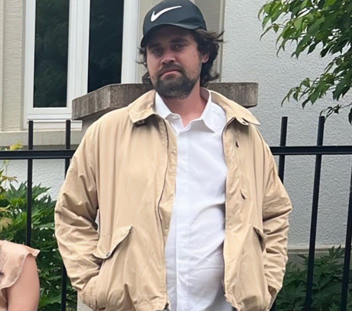 Man wearing beige jacket and black Nike cap standing outdoors near a fence referencing Conan O’Brien stopped 911 call topic.