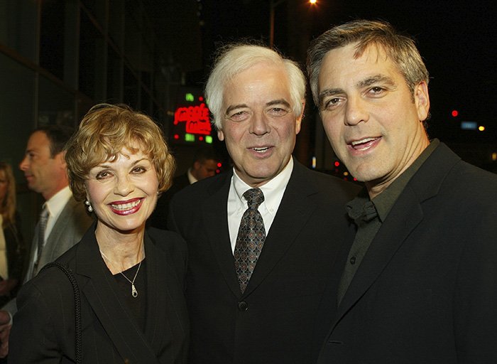 George Clooney at an event, smiling with two other people, highlighting tribute after sister Ada passes away at 65.
