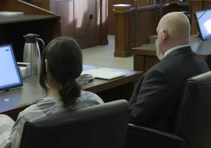 Trans Muslim woman sitting in courtroom next to lawyer during sentencing hearing after parents' passing case.
