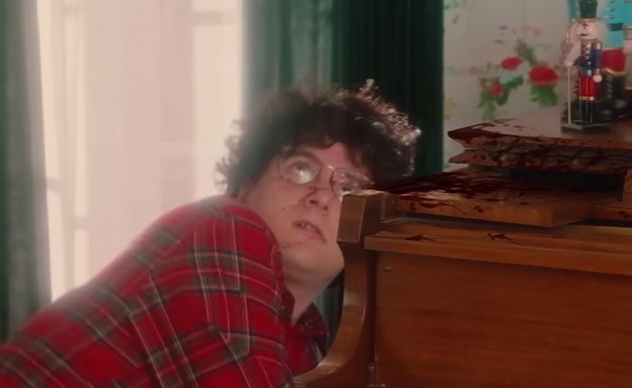 Man in red plaid shirt looking up, bloodied piano wood, scene from SNL Home Alone parody with Ariana Grande twist