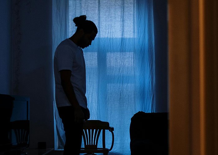 Man standing alone in a dimly lit room, appearing deep in thought about fianc&eacute;e&rsquo;s unexpected request before wedding.