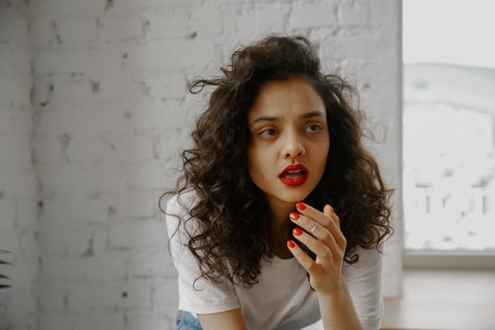 Young woman with curly hair and red lipstick looking uncertain, reflecting on affair partner's baby and complex family ties.