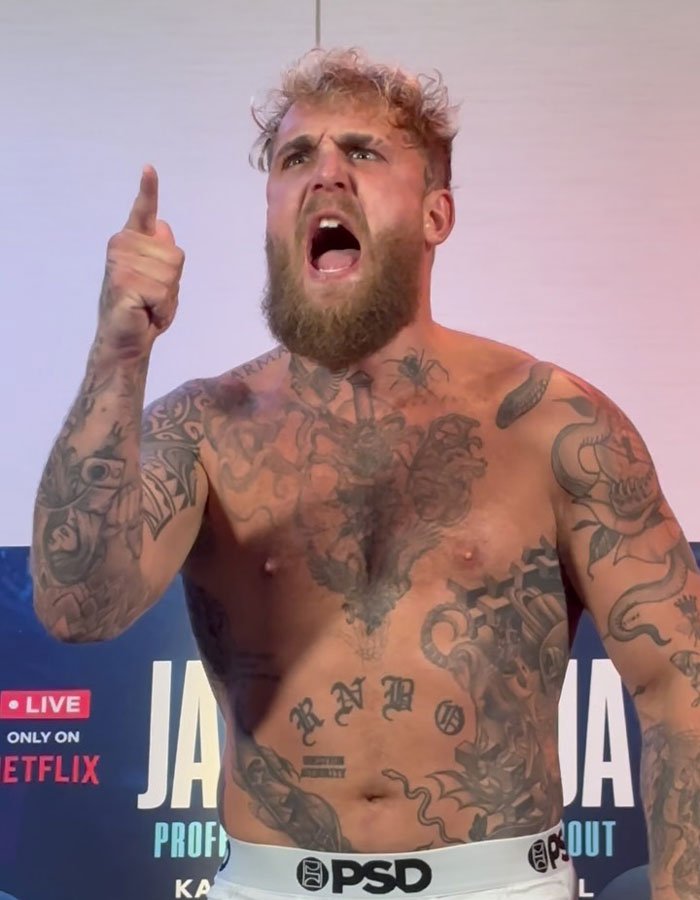 Jake Paul shirtless and tattooed, shouting with a raised finger during a live event.