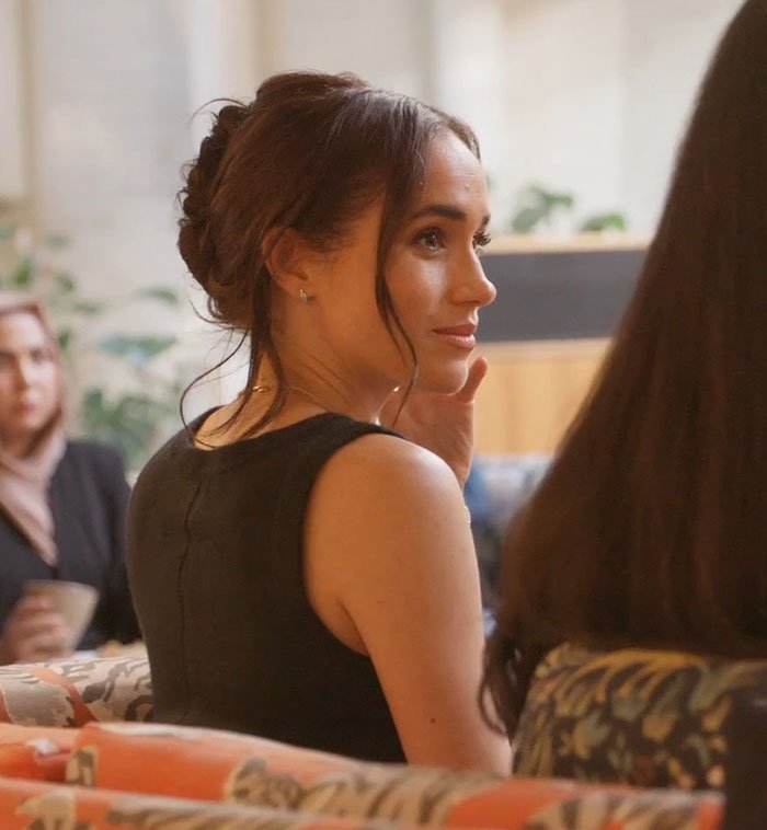Meghan Markle in a black dress sitting indoors with an attentive expression, related to Prince Harry holiday snap manipulation.